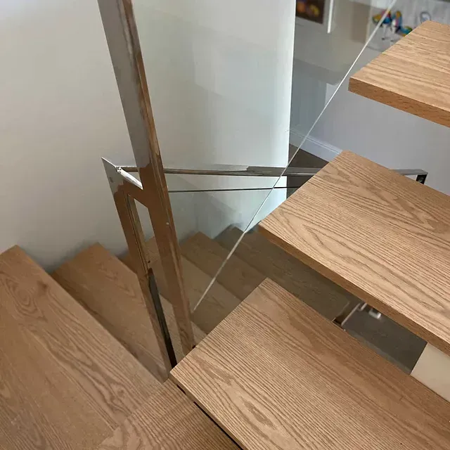 Un primer plano de una escalera de madera con barandilla de vidrio.