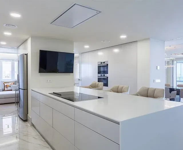 Una cocina con gabinetes blancos y un televisor de pantalla plana en la pared.