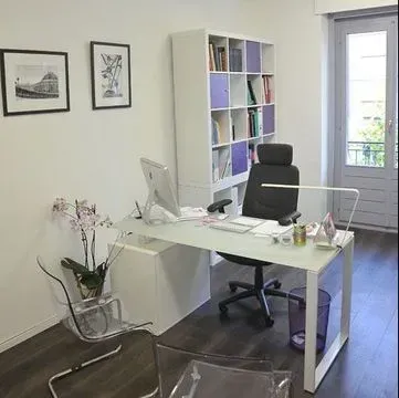 Bureau avec bureau blanc, bibliothèque et deux tableaux encadrés au mur. Des chaises transparentes sont placées devant.