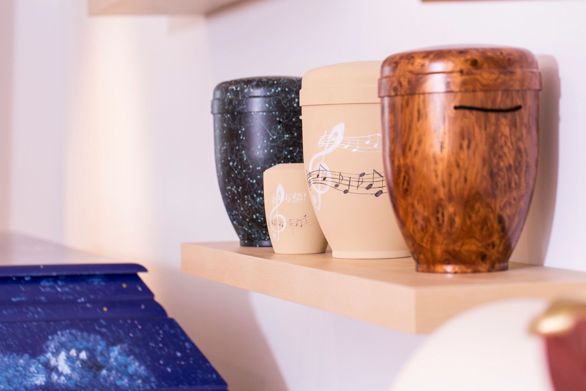 Drei Urnen stehen auf einem Holzregal in einem Raum.