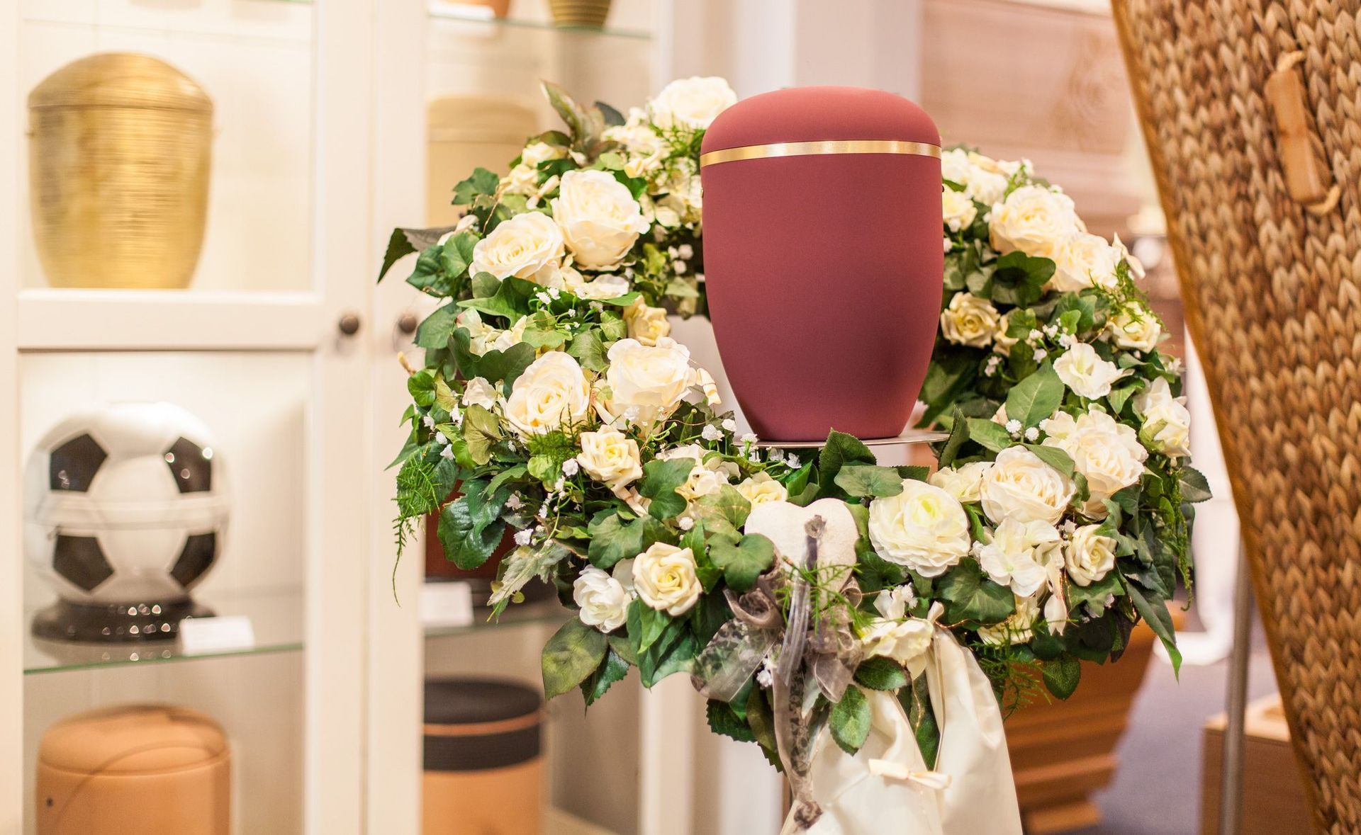 Auf einer roten Urne steht ein Kranz aus weißen Rosen.