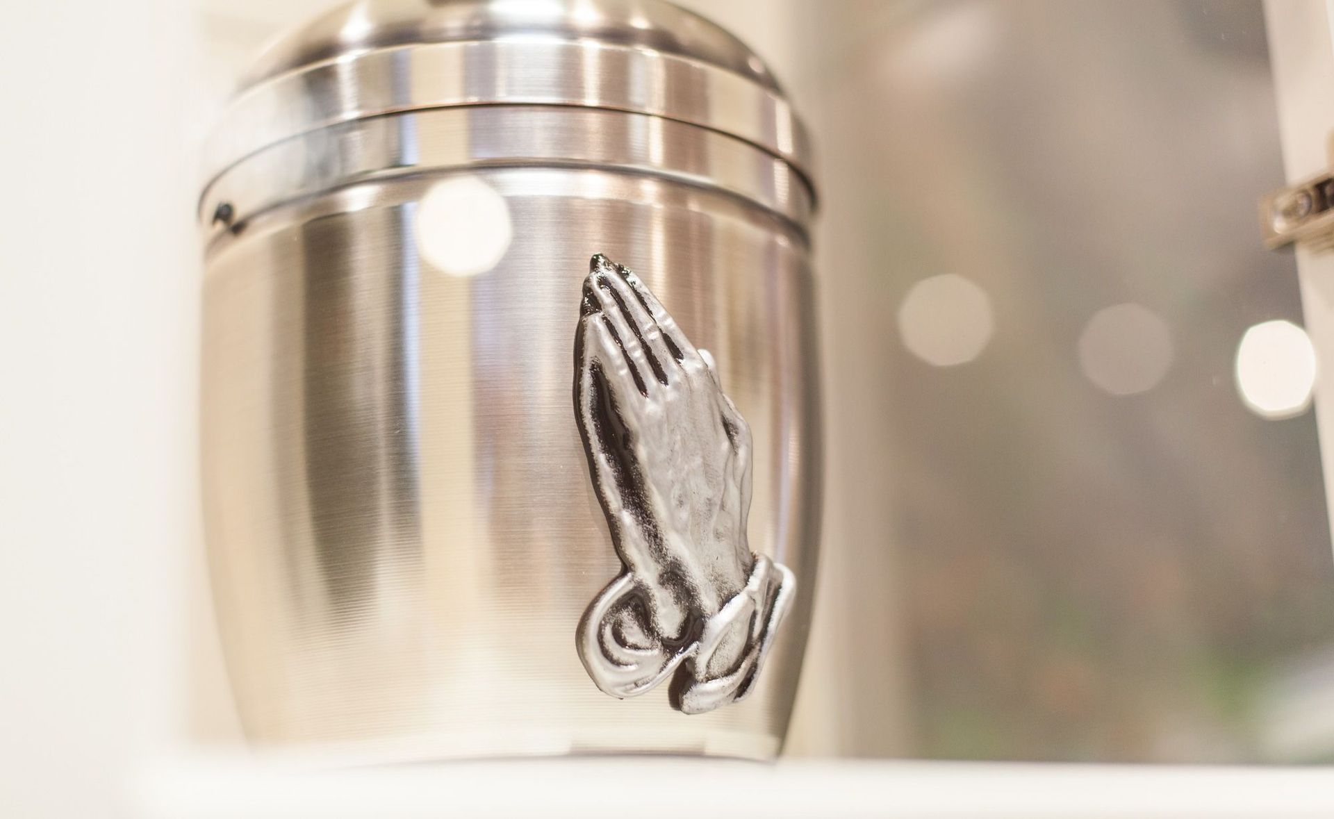 Auf einem Regal steht eine silberne Urne mit betenden Händen.