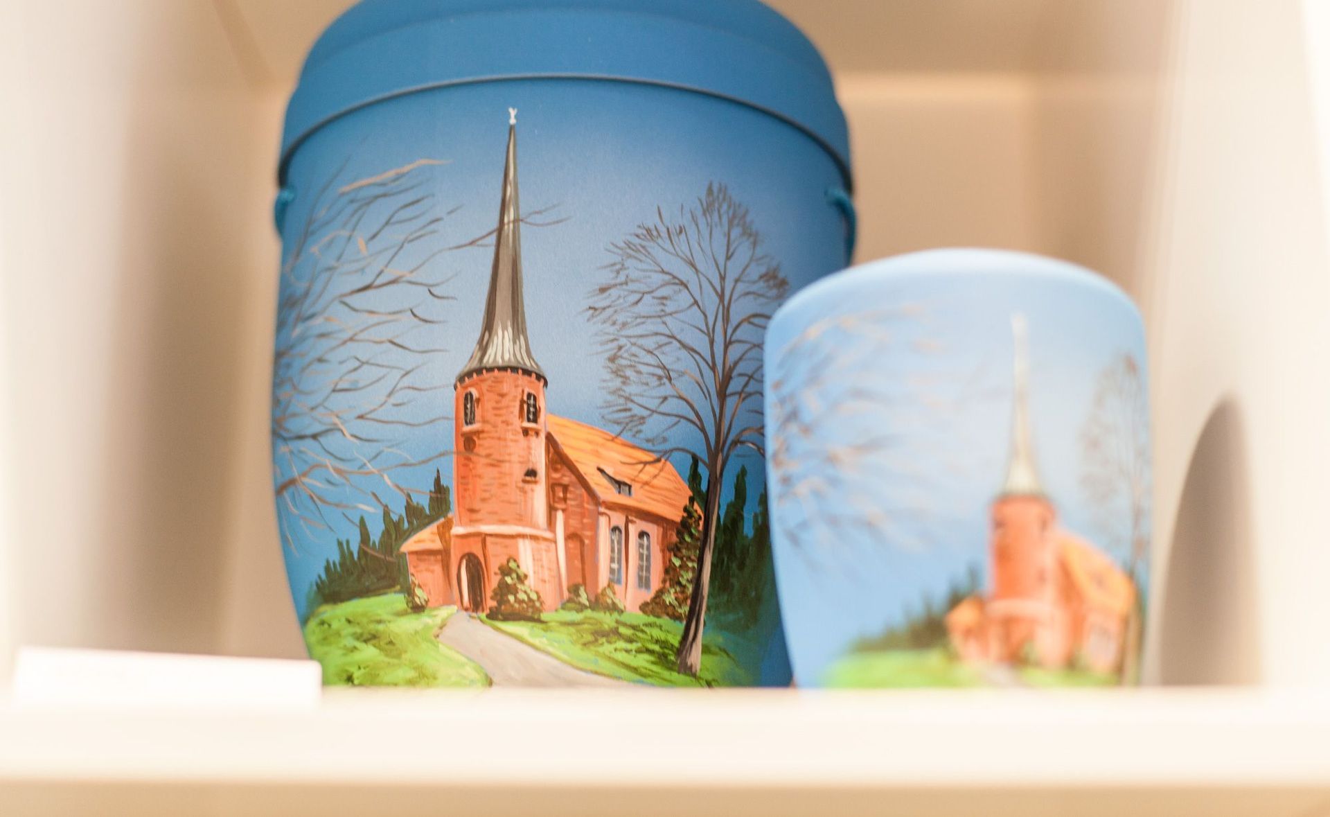 Auf einem Regal stehen zwei Urnen mit dem Bild einer Kirche darauf.