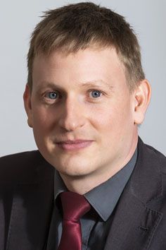 Ein Mann in Anzug und Krawatte lächelt in die Kamera.