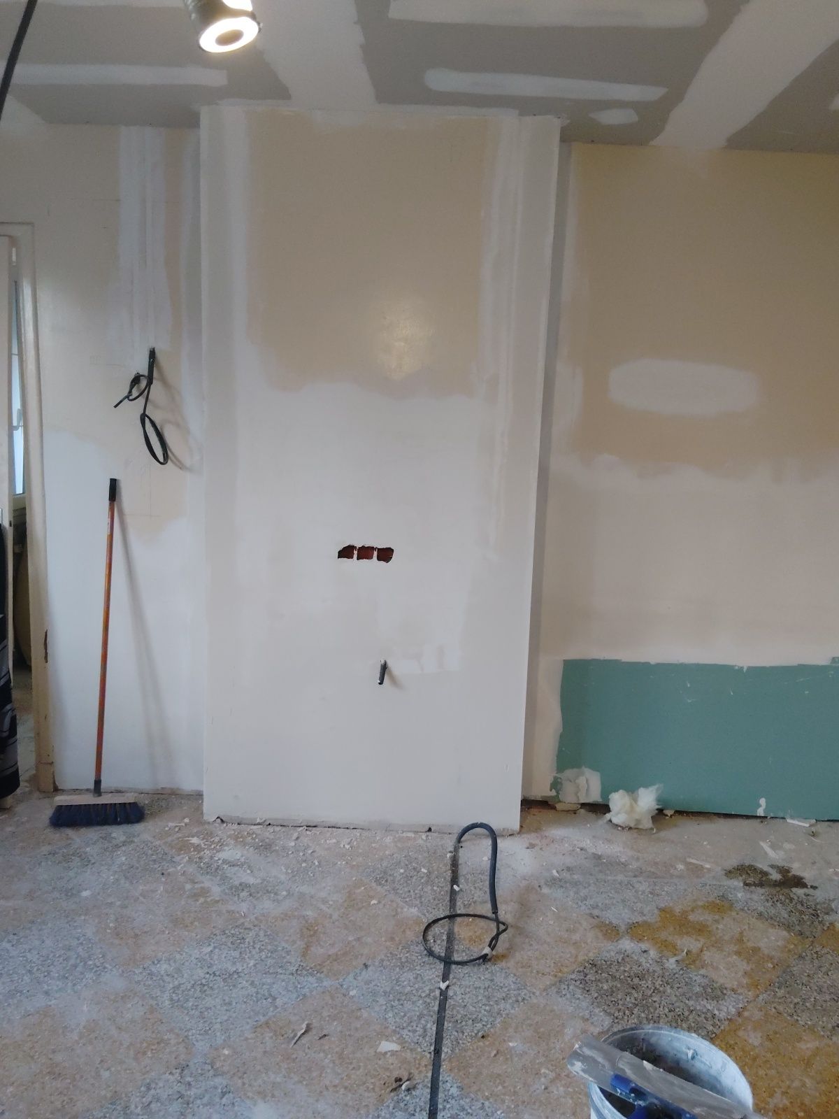 Pièce en cours de rénovation, avec des plaques de plâtre réparées, des fils électriques apparents et des débris au sol.