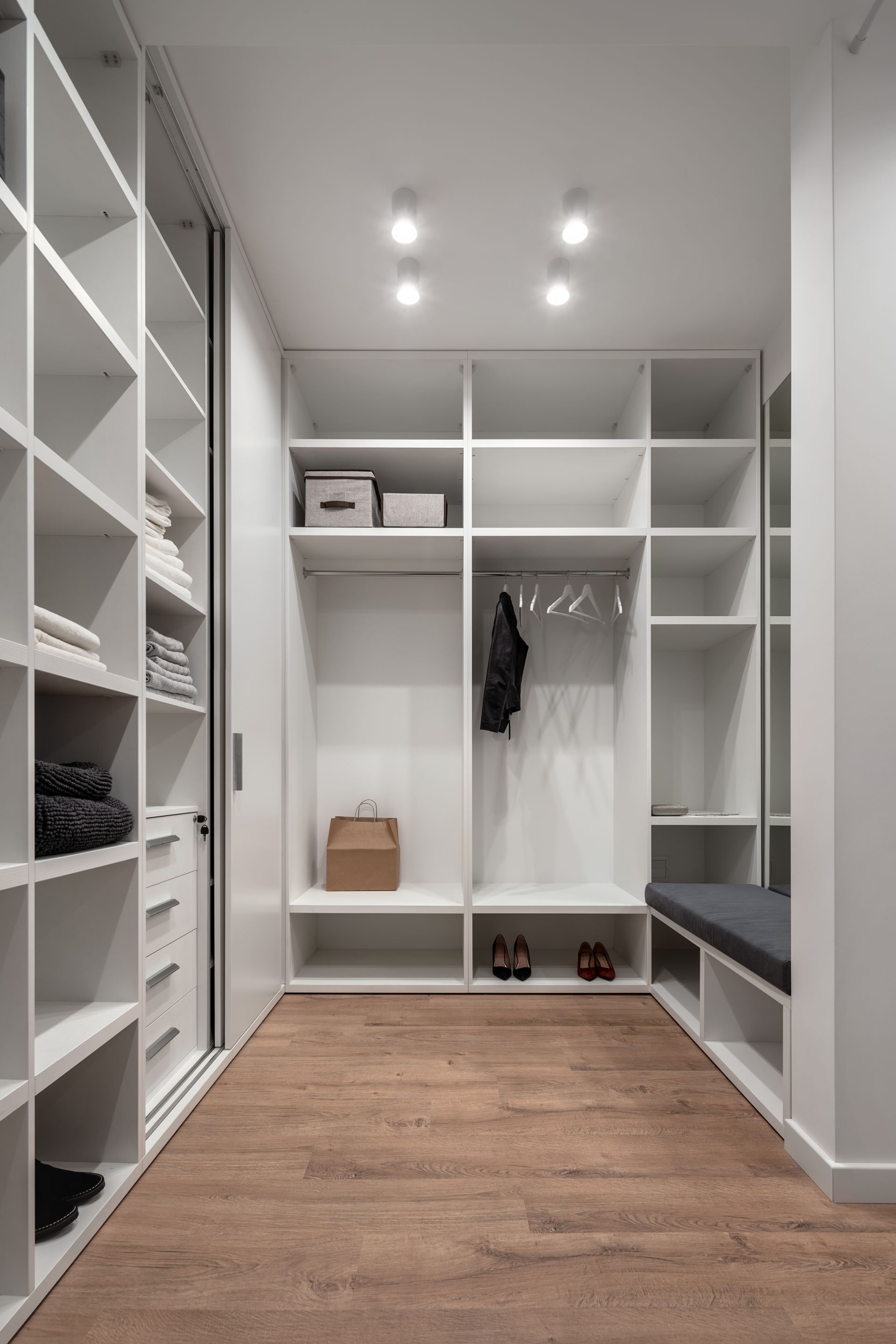 Dressing-room avec des étagères intégrées, penderie et parquet, éclairé par des spots encastrés au plafond.