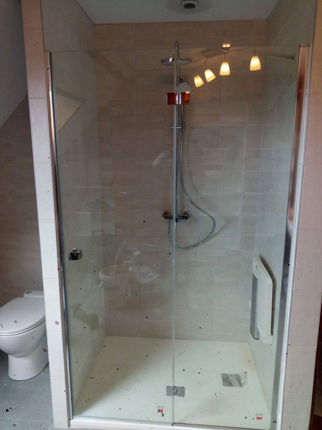 Petite salle de bains carrelée avec une cabine de douche en verre, des équipements et des toilettes visibles à gauche.