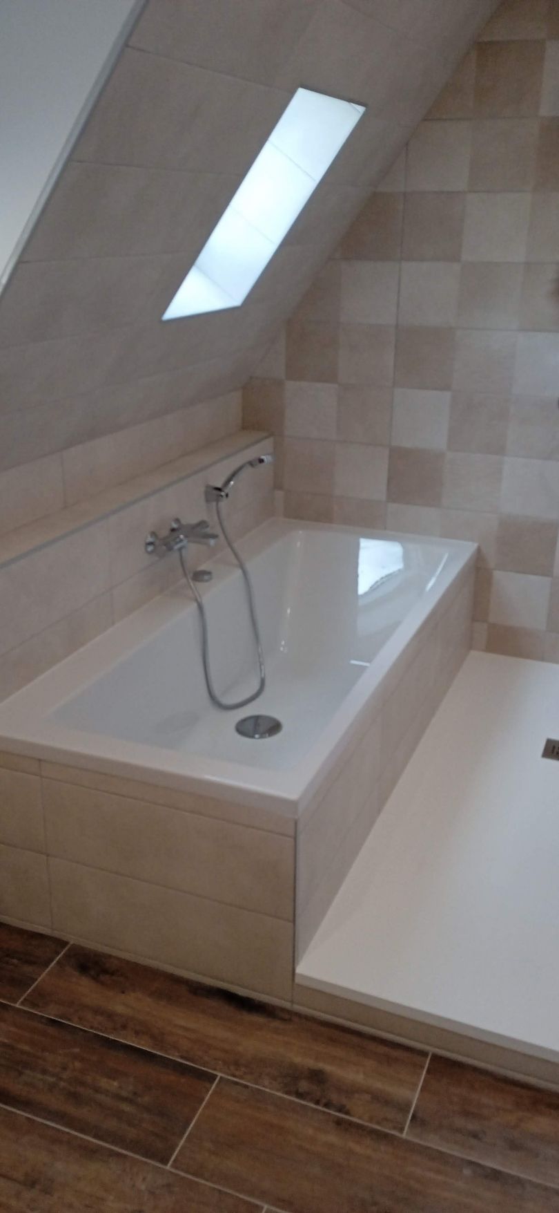 Salle de bains moderne avec baignoire, fenêtre de toit inclinée et murs carrelés.