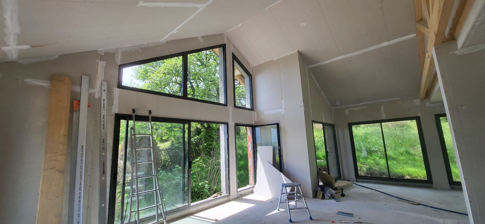 Intérieur moderne en cours de finition, avec des fenêtres du sol au plafond, des murs apparents et des matériaux de construction.
