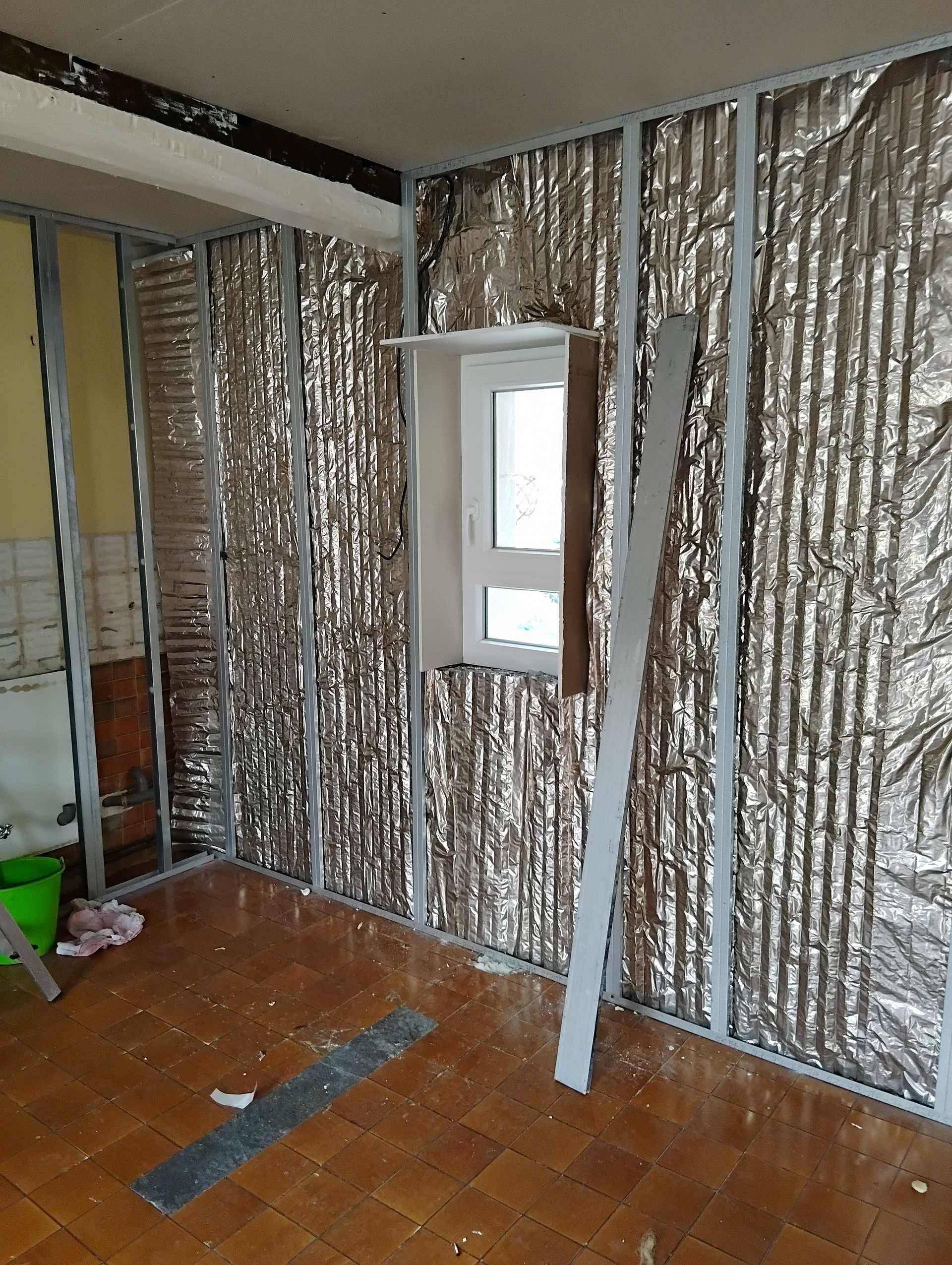 Pièce avec une isolation argentée sur les murs, une petite fenêtre, un sol carrelé et des outils.