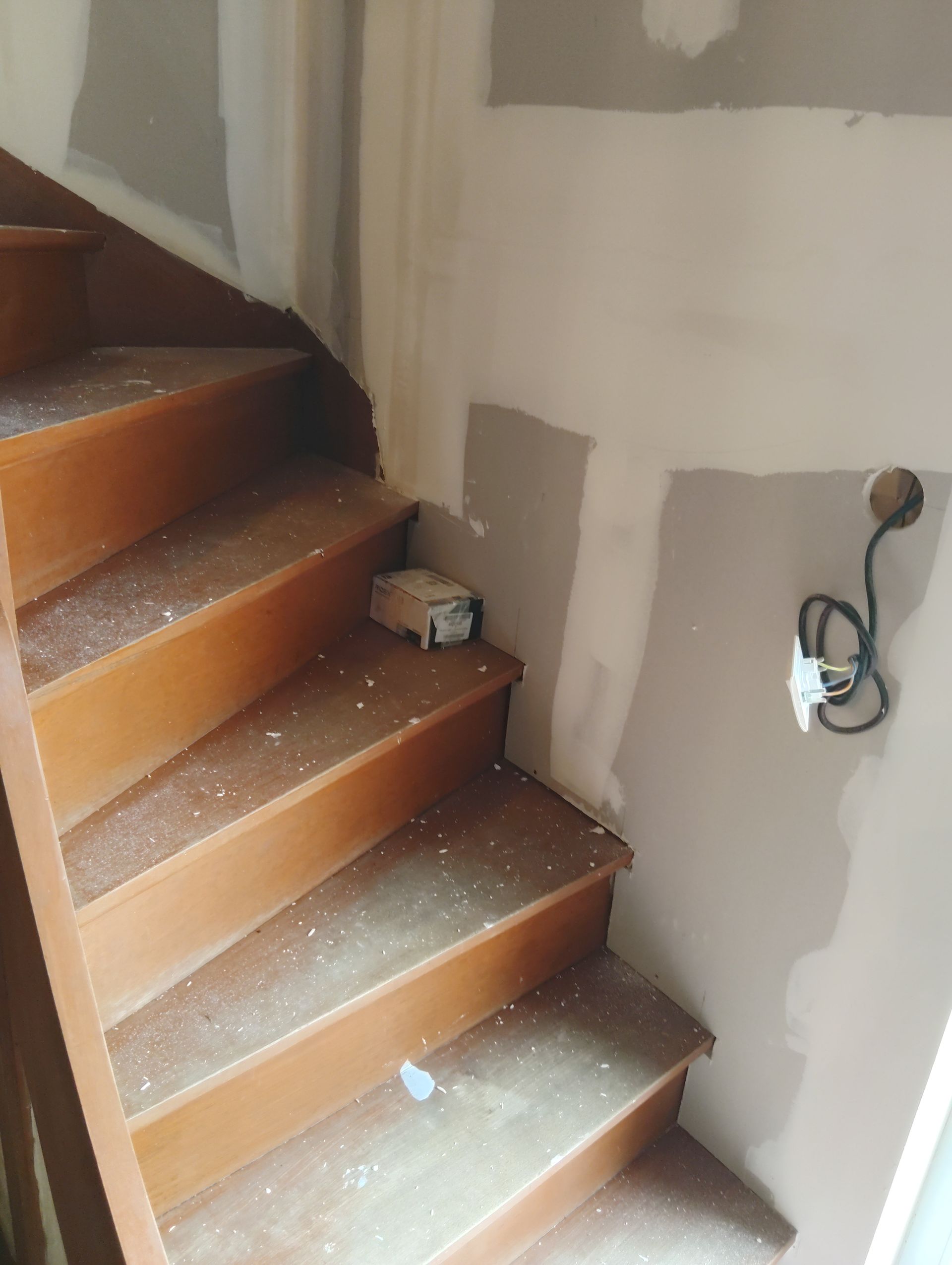 Escalier en construction avec des marches, de la poussière sur les marches et des fils électriques apparents sur le mur.
