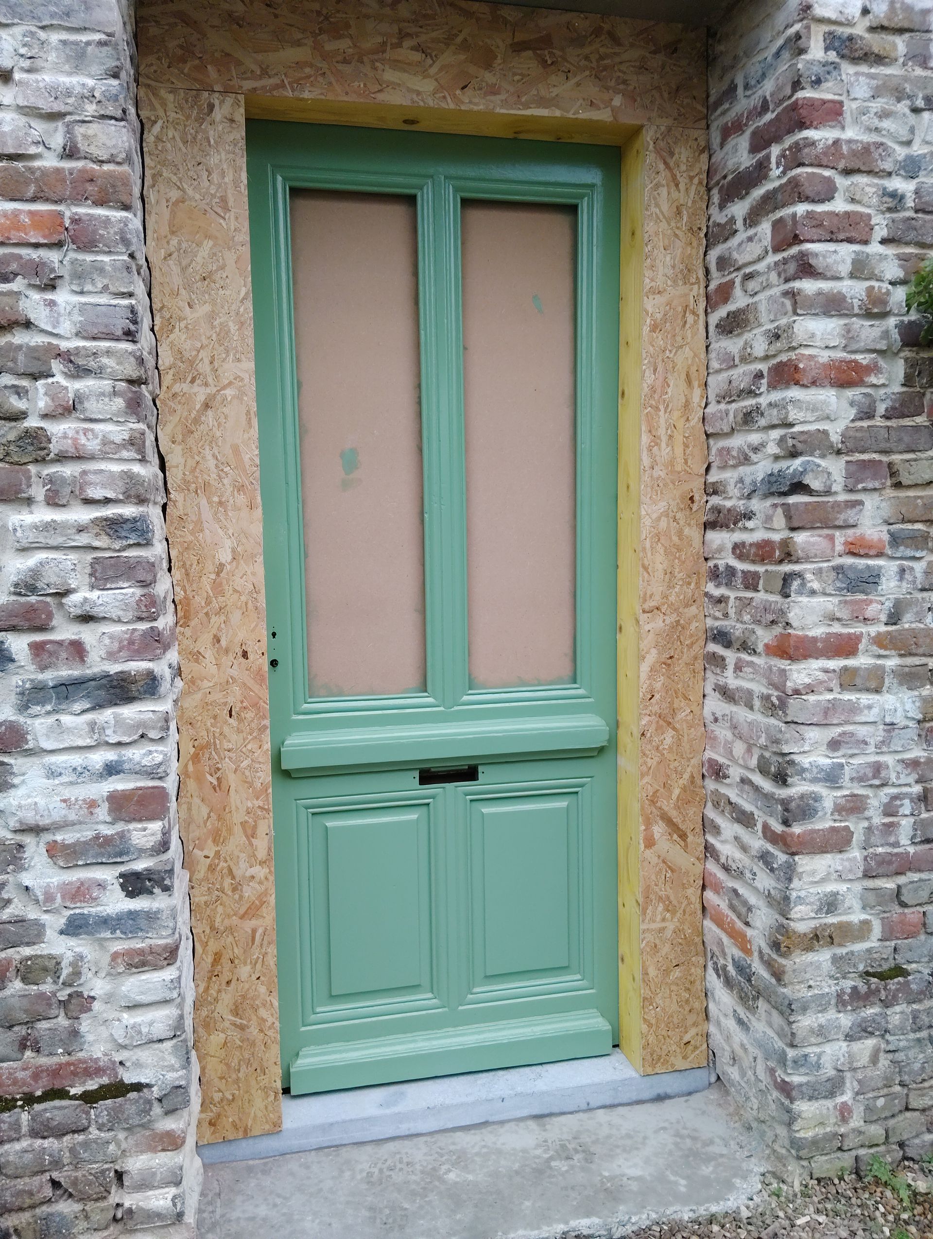 Porte en bois peinte, encastrée dans un mur de briques, avec des vitres dépolies et un seuil en pierre.