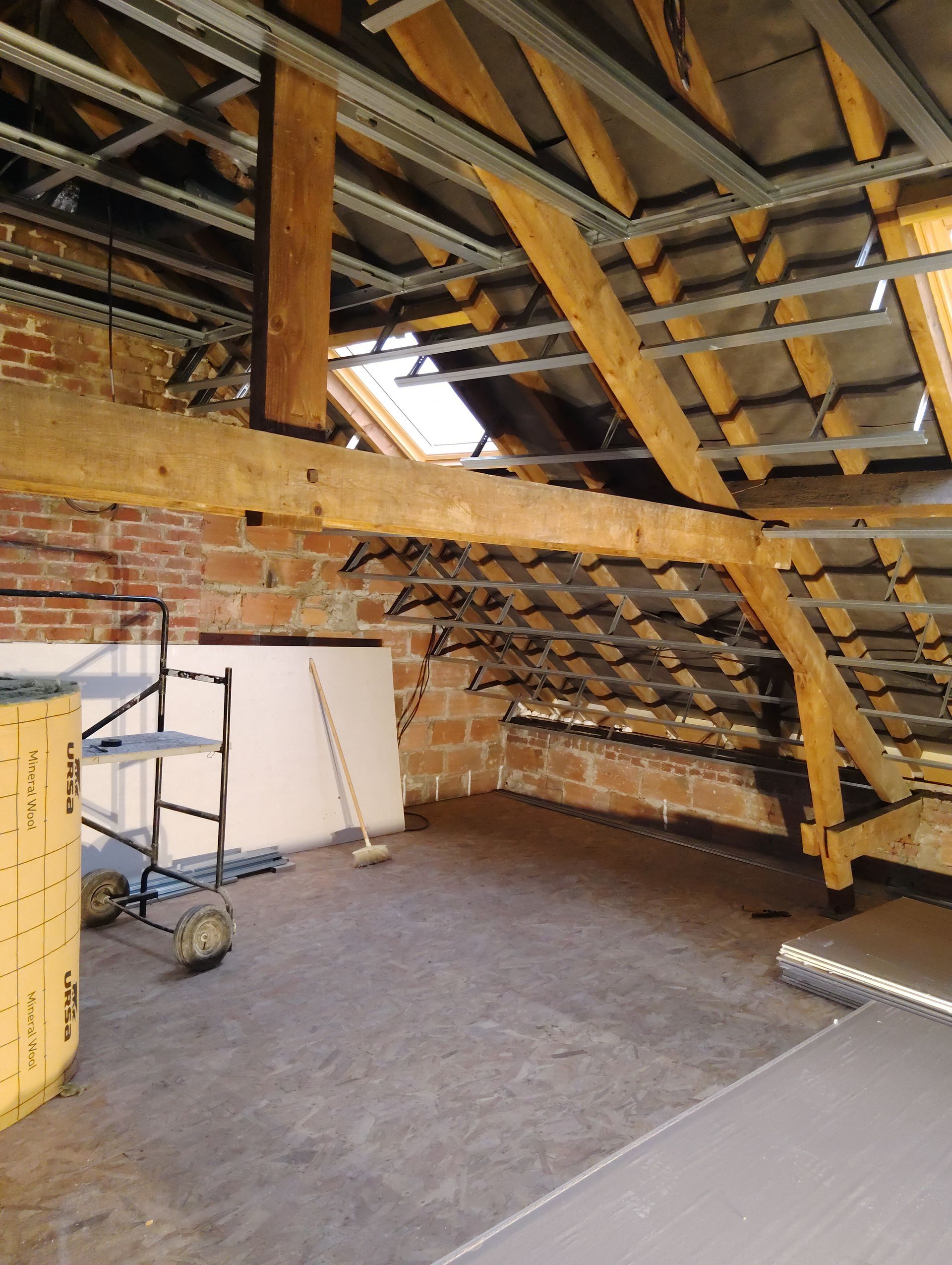 Intérieur de grenier avec des poutres en bois apparentes, des murs en briques, échafaudages et des matériaux de construction au sol.