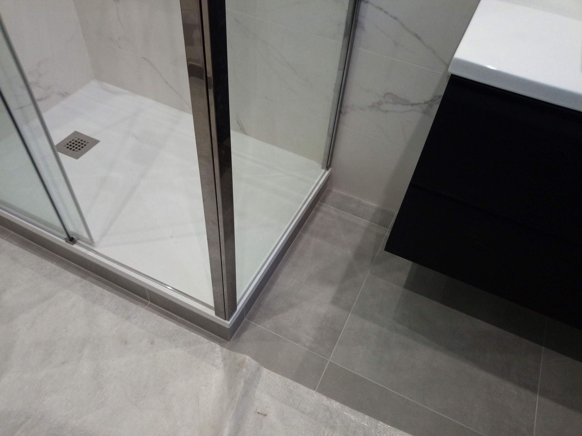 Paroi de douche en verre à côté d’un meuble-lavabo, dans une salle de bains carrelée.