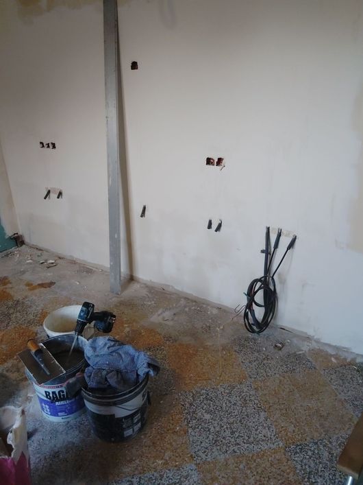 Pièce partiellement rénovée, avec des murs nus, des pots de peinture, des outils et des fils électriques au sol.