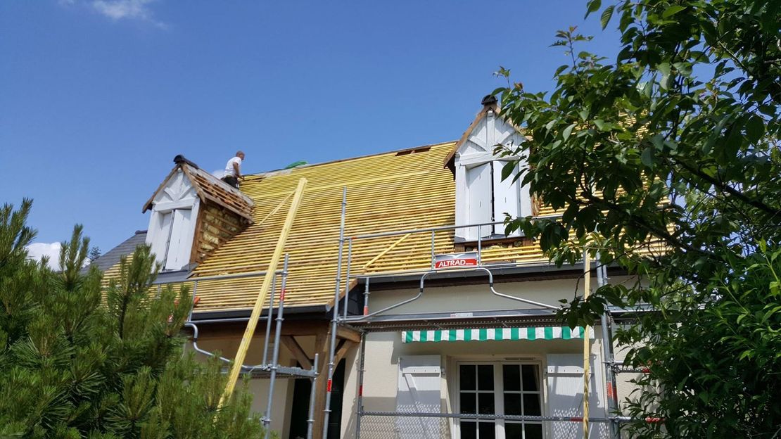 Un ouvrier réalise la couverture d'un toit sur une charpente extérieure en bois
