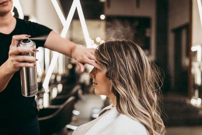 Eine Stylistin trägt in einem Salon Haarspray auf das Haar einer Kundin auf.