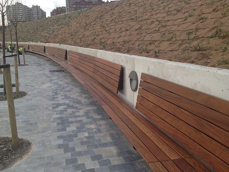 Un banco largo de madera está junto a una pared de hormigón.