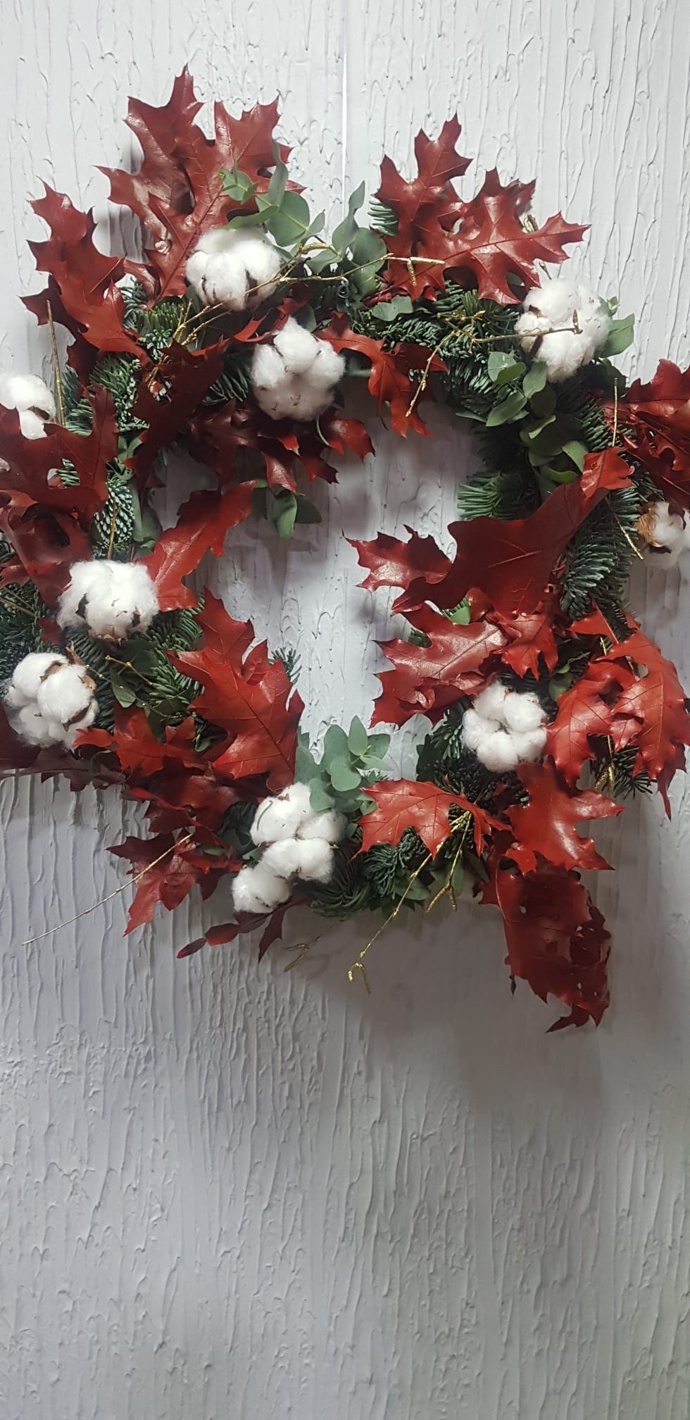 Una corona navideña con hojas rojas y bolas de algodón blancas cuelga de una pared blanca.
