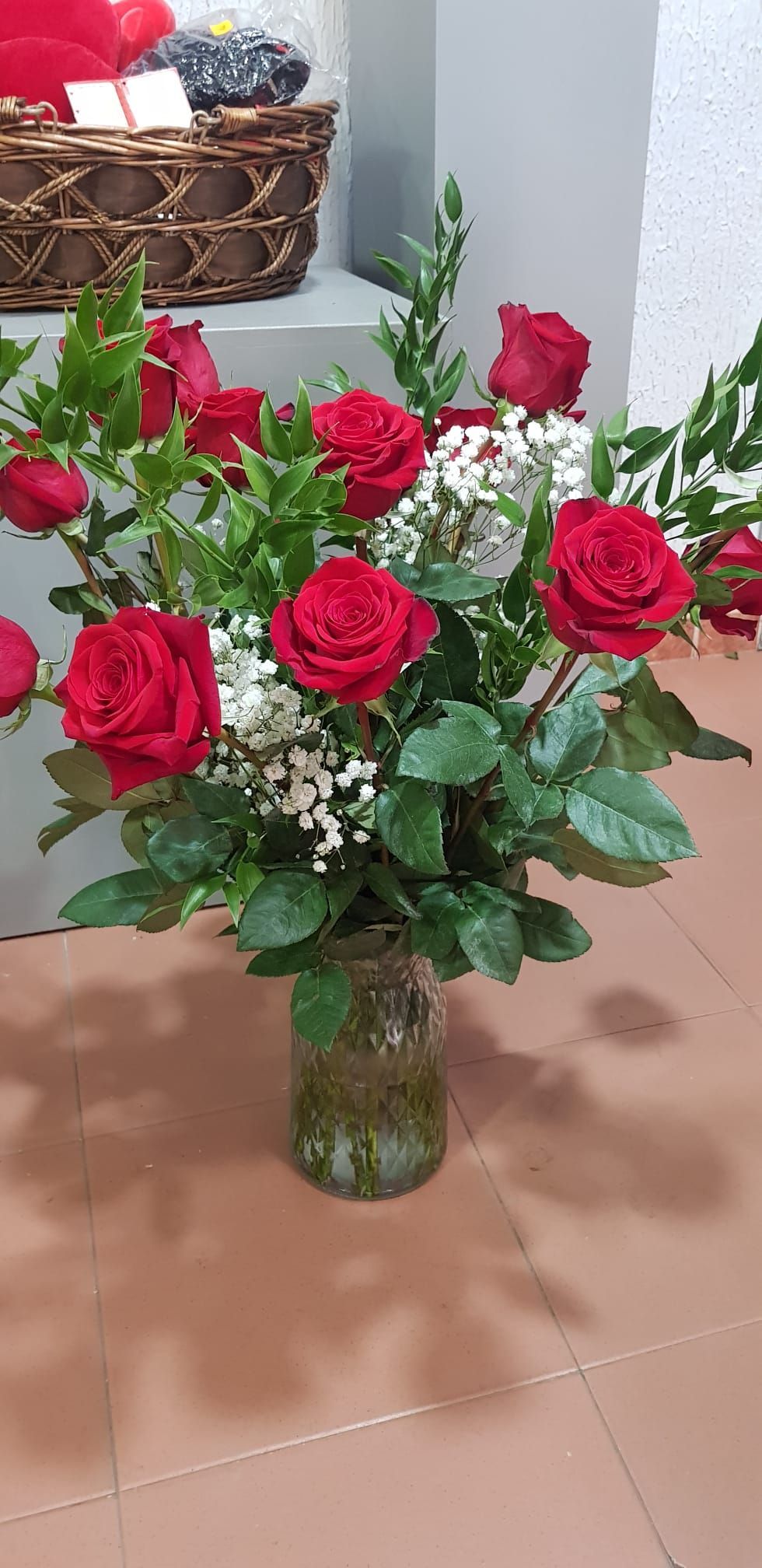 Un jarrón lleno de rosas rojas y flores de bebé se encuentra sobre un suelo de baldosas.