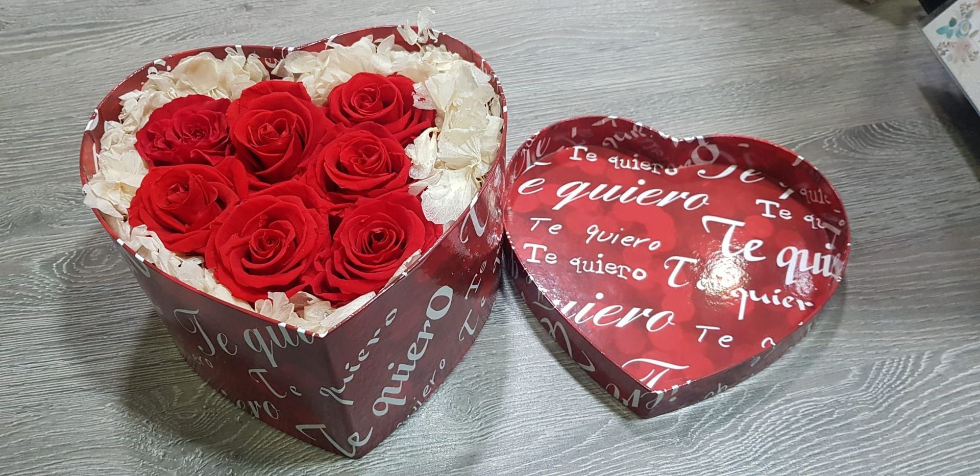 Una caja en forma de corazón llena de rosas rojas está sobre una mesa.