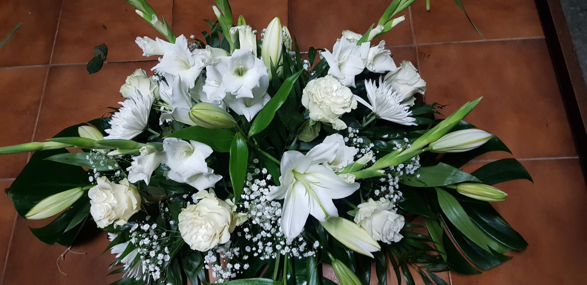 Un gran ramo de flores blancas reposa sobre un suelo de baldosas.