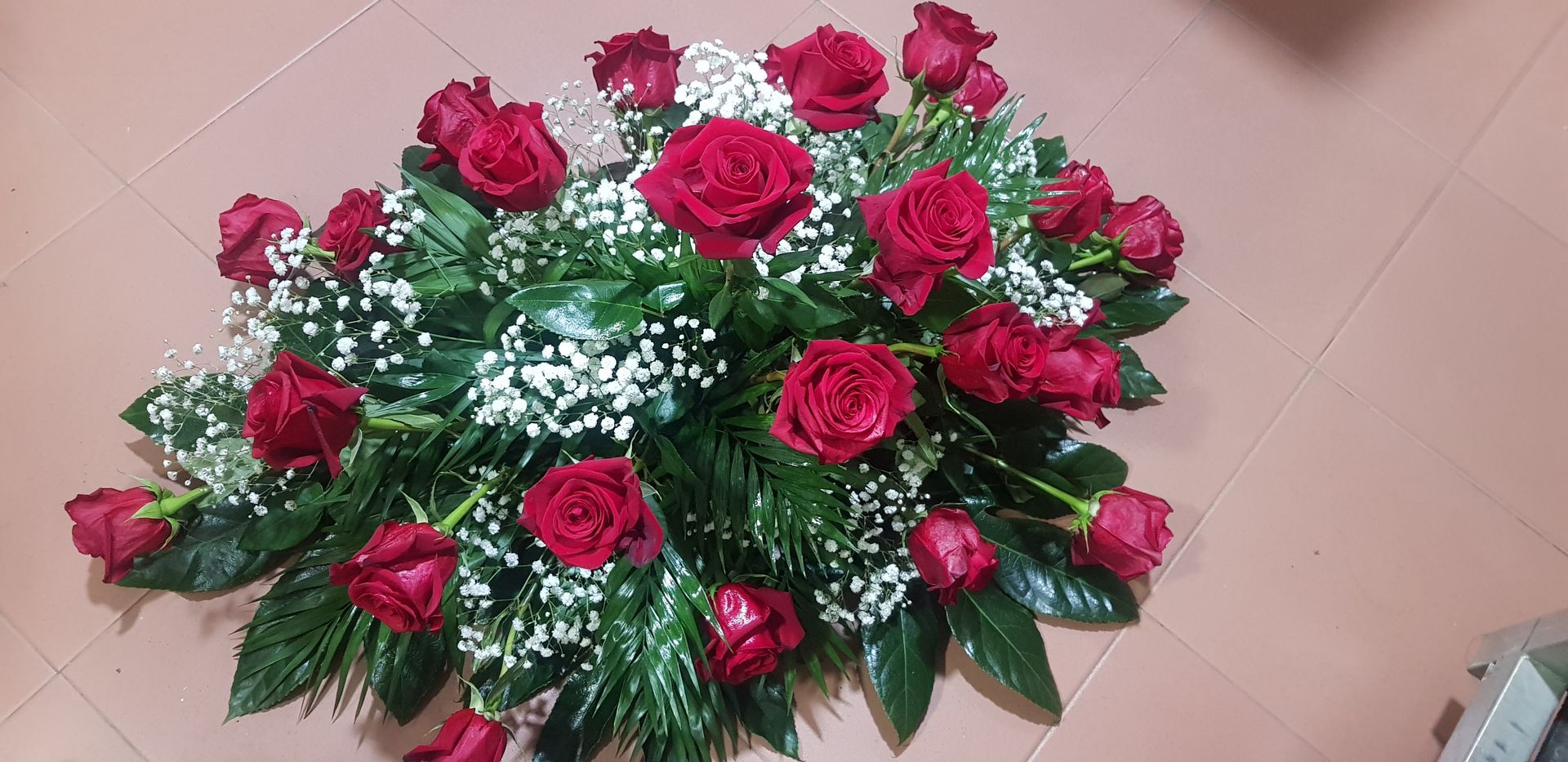 Un ramo de rosas rojas y flores de aliento está sobre un suelo de baldosas.