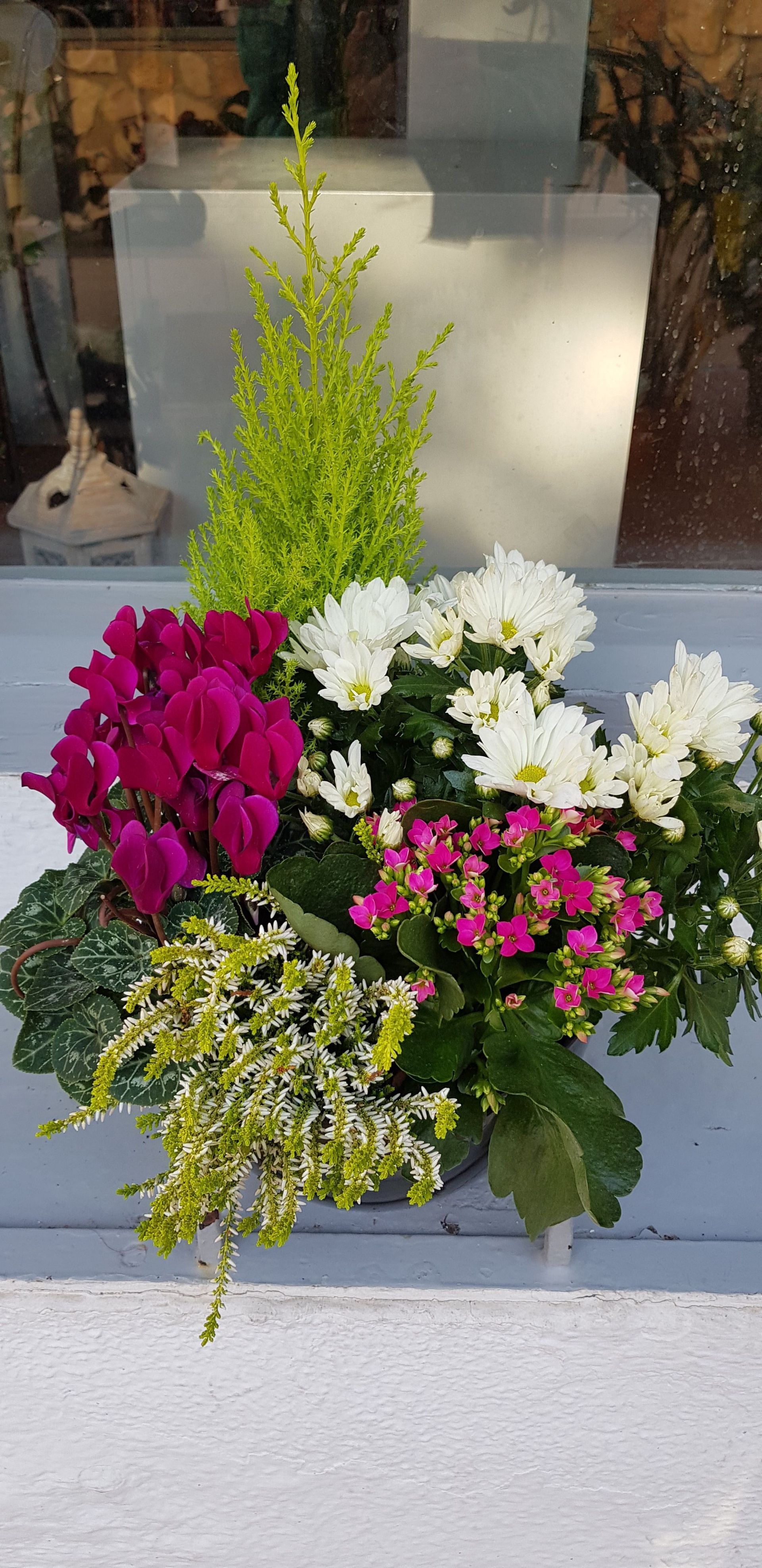Un jarrón lleno de flores y plantas está sobre una mesa.