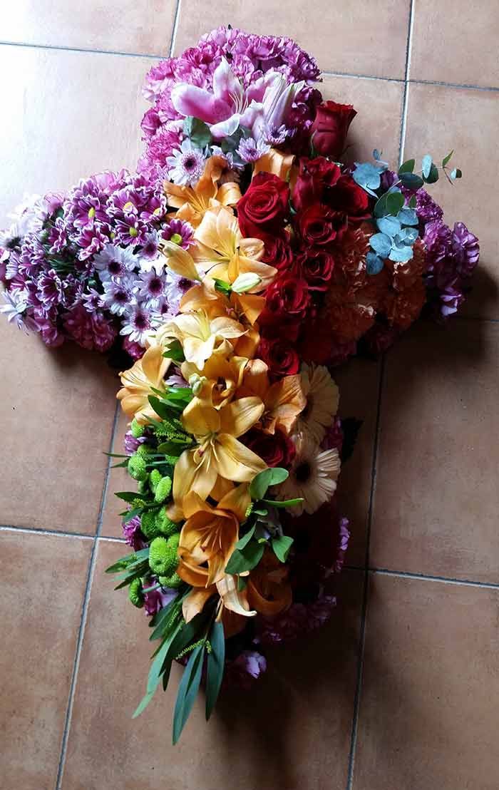 Una cruz hecha de flores reposa sobre un suelo de baldosas.