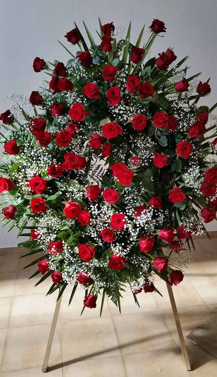 Una corona de rosas rojas y flores de aliento del bebé en un soporte.