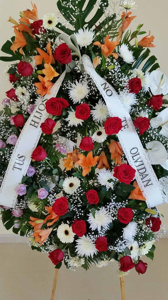 Una corona con rosas rojas y flores blancas con una cinta que dice 