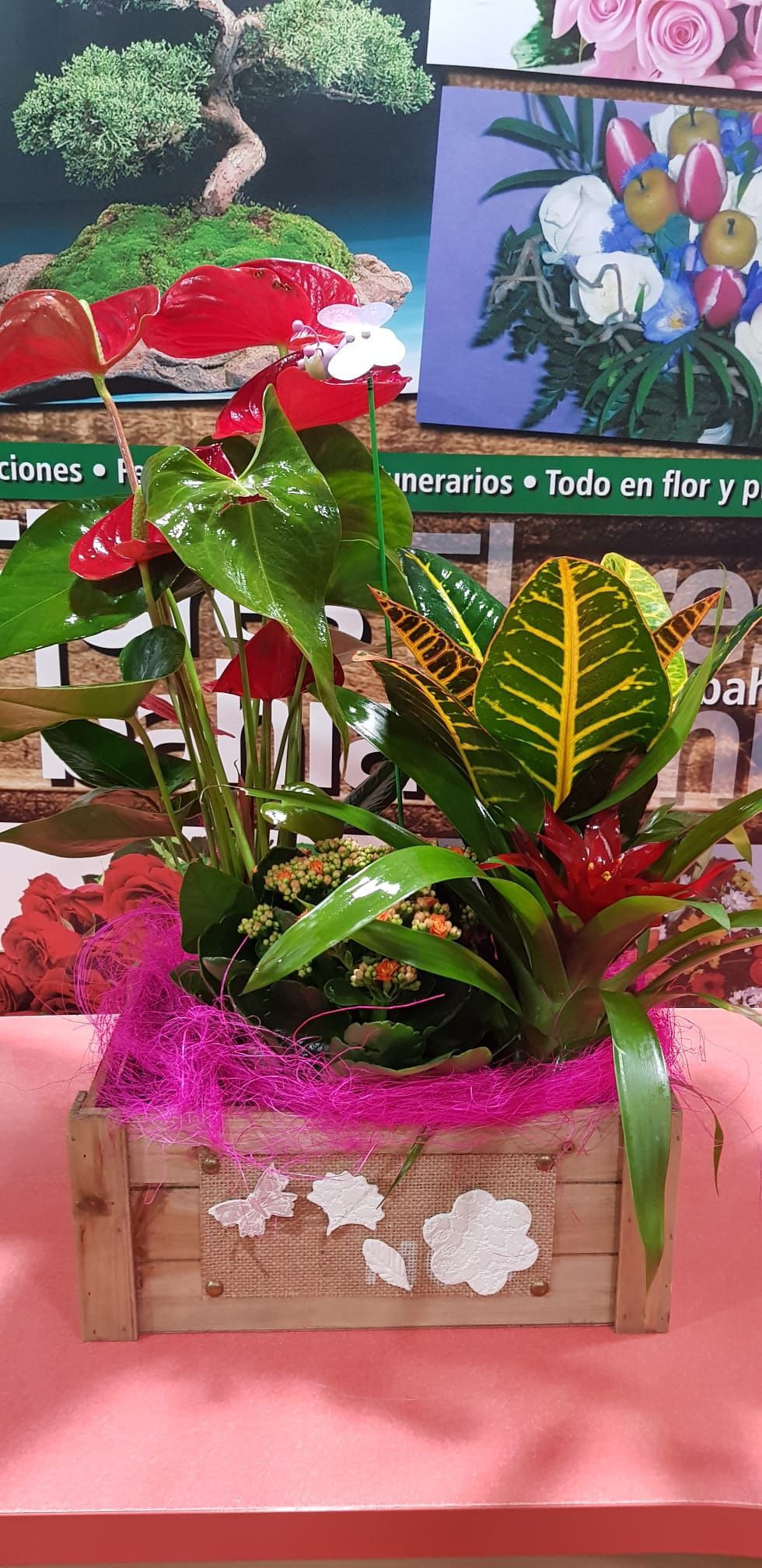 Una caja de madera llena de flores y plantas está sobre una mesa.