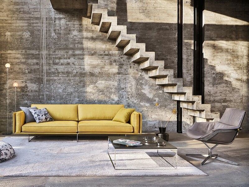 Un salon avec un canapé jaune, une chaise, une table basse et des escaliers.