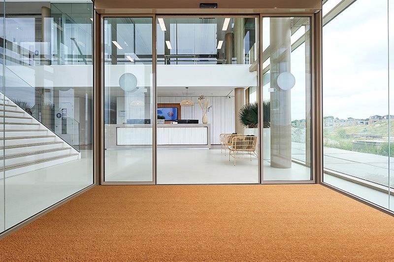 Un grand bâtiment avec une porte coulissante en verre et un tapis au sol.