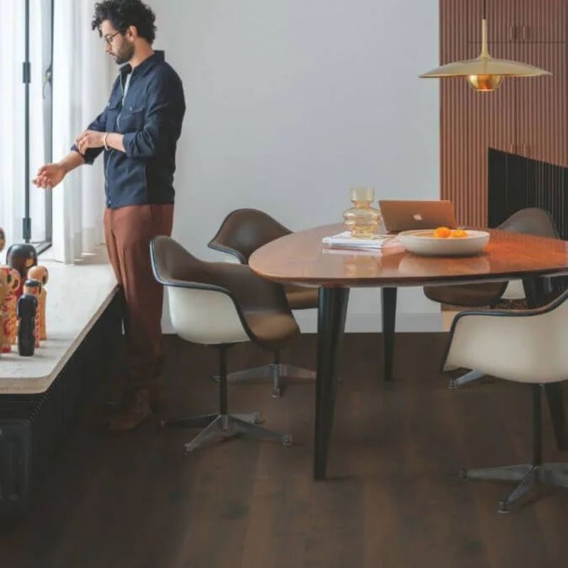 Un homme se tient dans un salon à côté d'une table et de chaises.