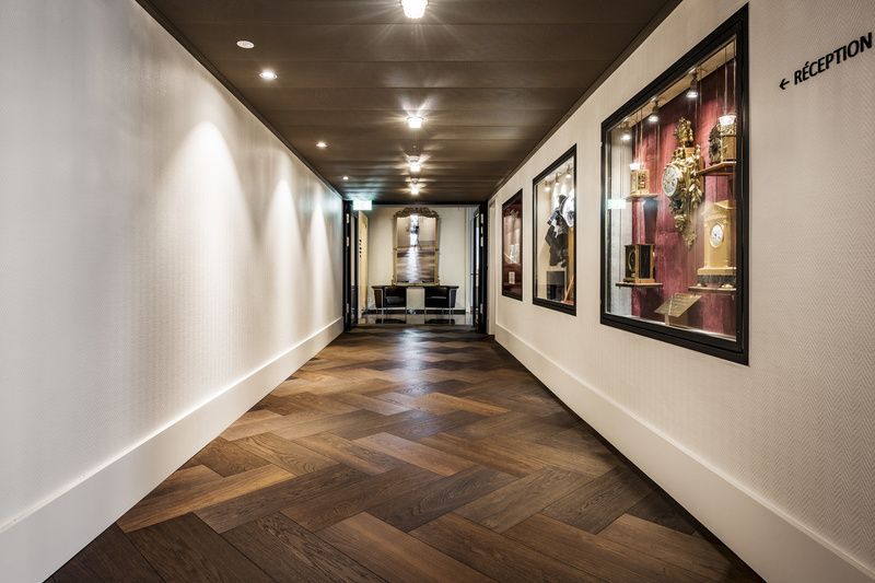 Un long couloir avec du parquet et un panneau de réception au mur.