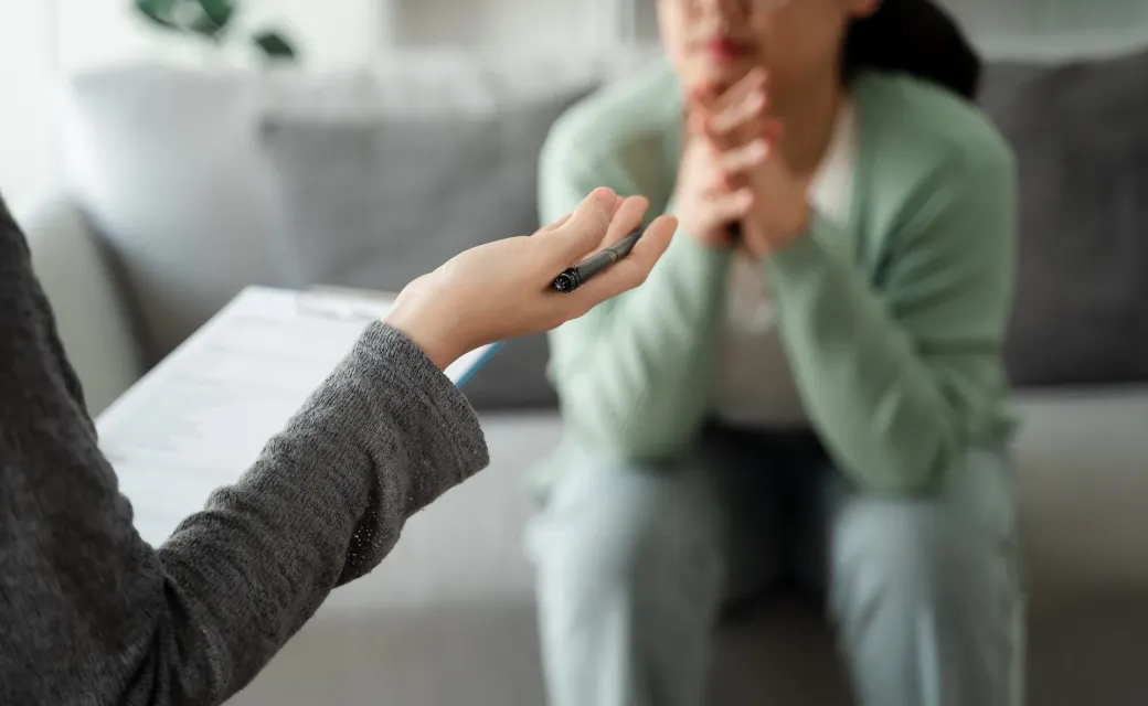 Terapeuta y paciente en una sesión de terapia. Una mano con un bolígrafo señala a una persona sentada.
