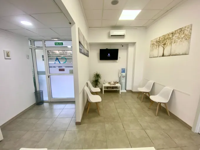 Sala de espera con sillas blancas, TV, arte, mesa pequeña y un pequeño árbol de Navidad.