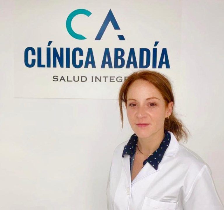 Mujer con bata blanca junto al cartel de 