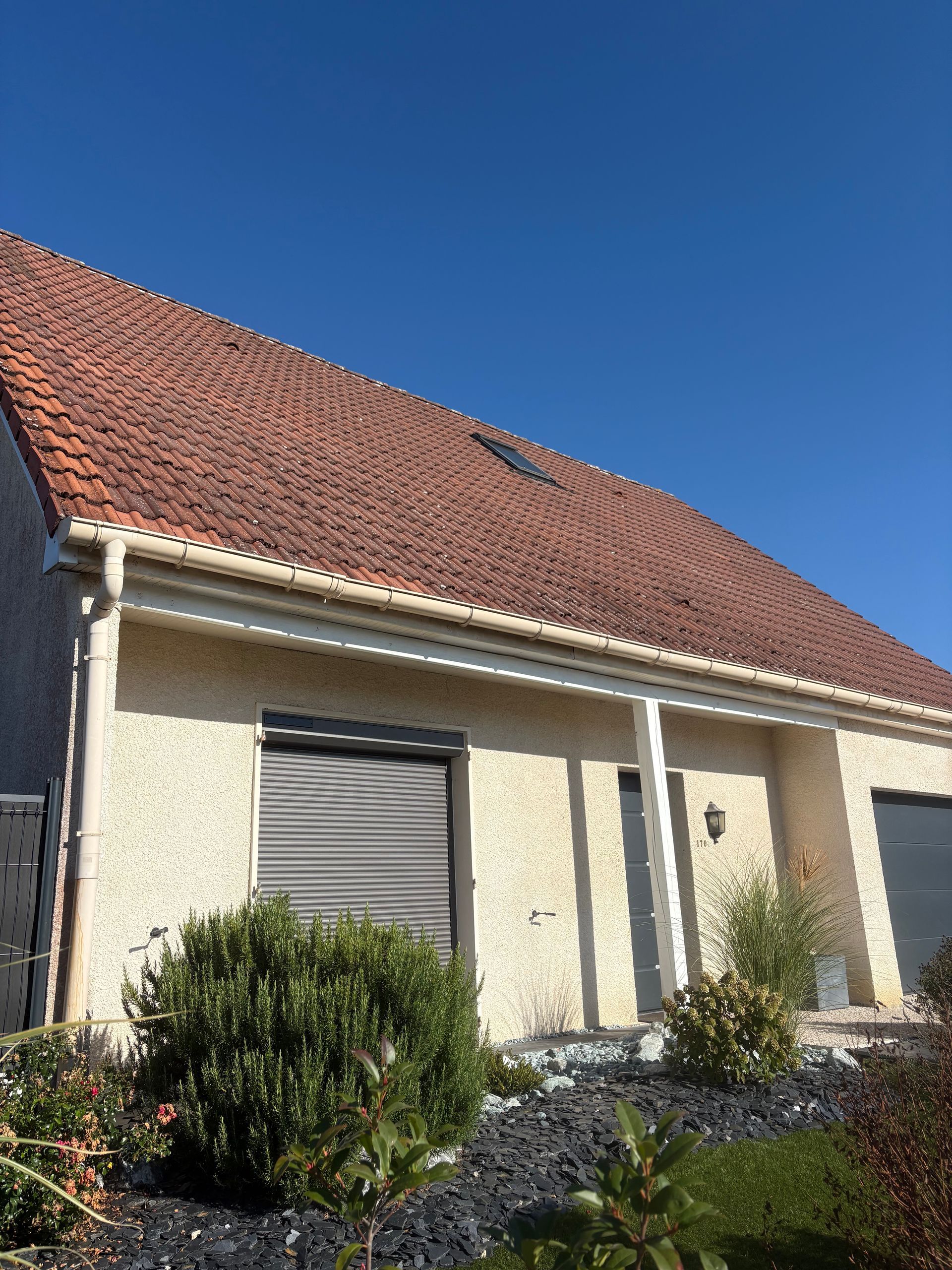 Maison en stuc beige avec toit de tuiles rouges et ciel bleu.