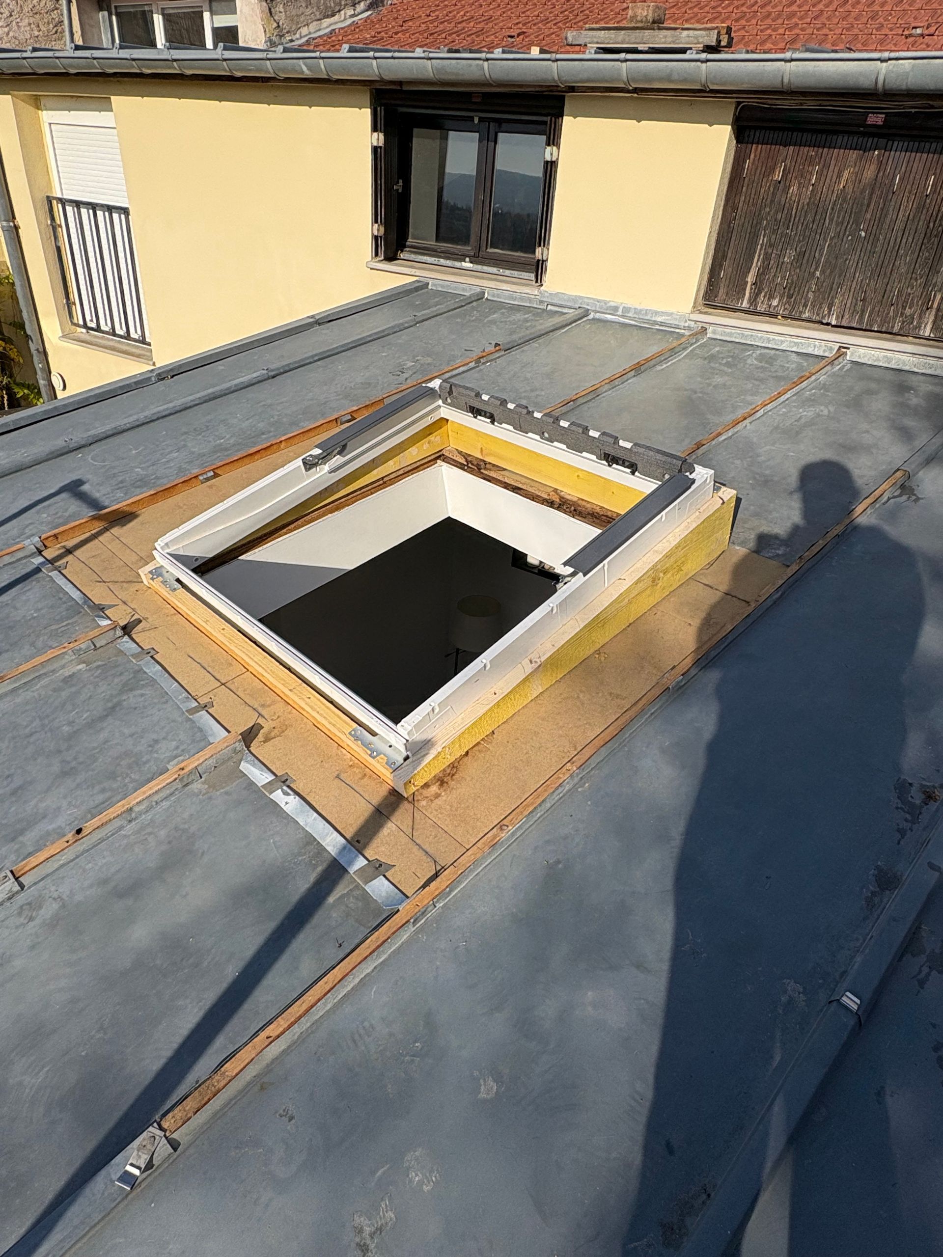 Toiture avec puits de lumière en cours d'installation ; la toiture est grise et le cadre du puits de lumière est blanc.