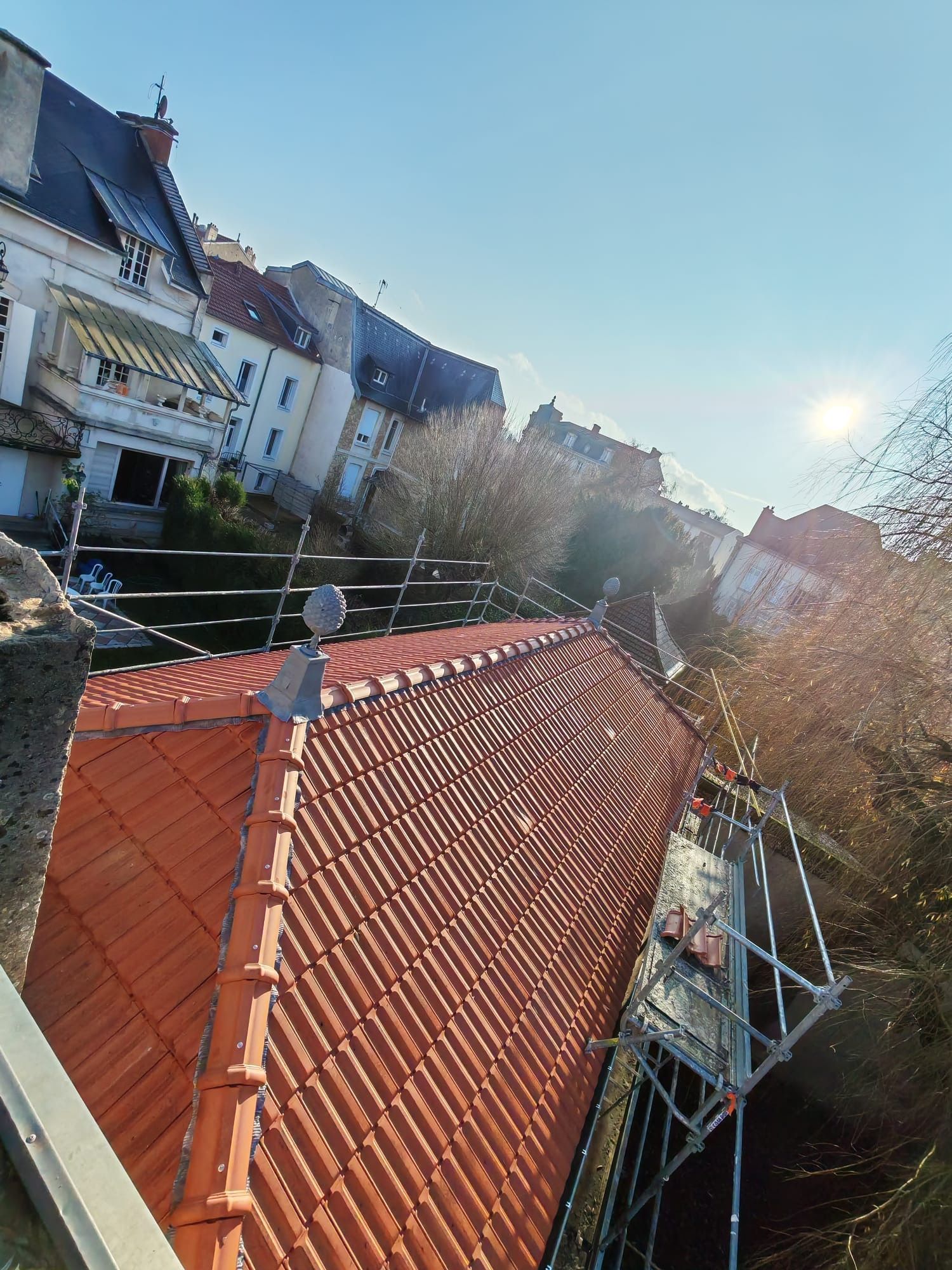 Toit de tuiles rouges avec un puits de lumière, maisons et voitures en arrière-plan.