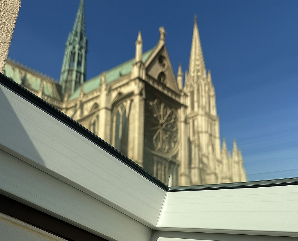 Extérieur de la cathédrale avec une façade claire et de hautes flèches se détachant sur un ciel bleu, vu depuis une fenêtre.