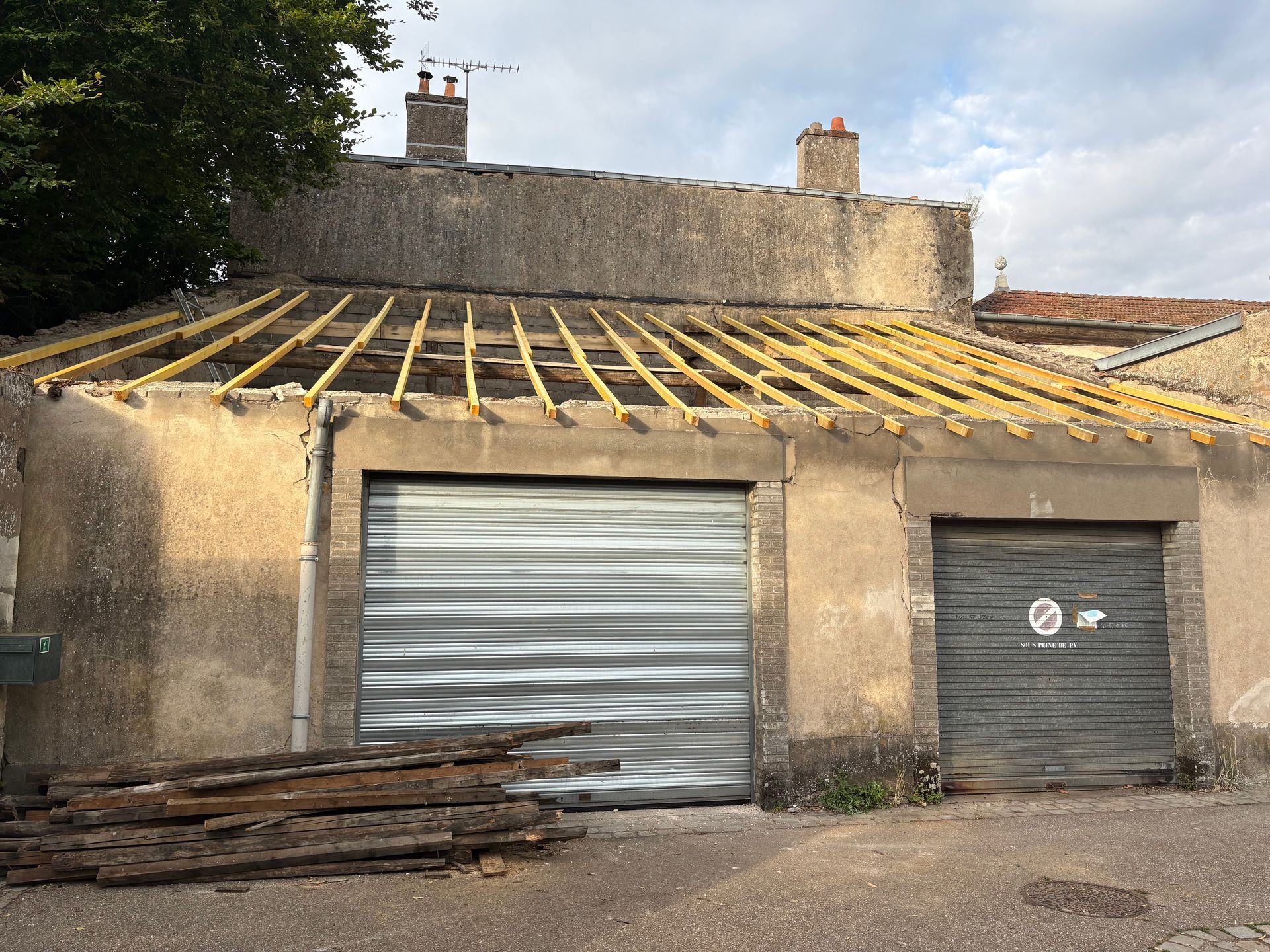 Bâtiment avec un toit partiellement arraché et deux portes de garage. Débris de bois au premier plan.