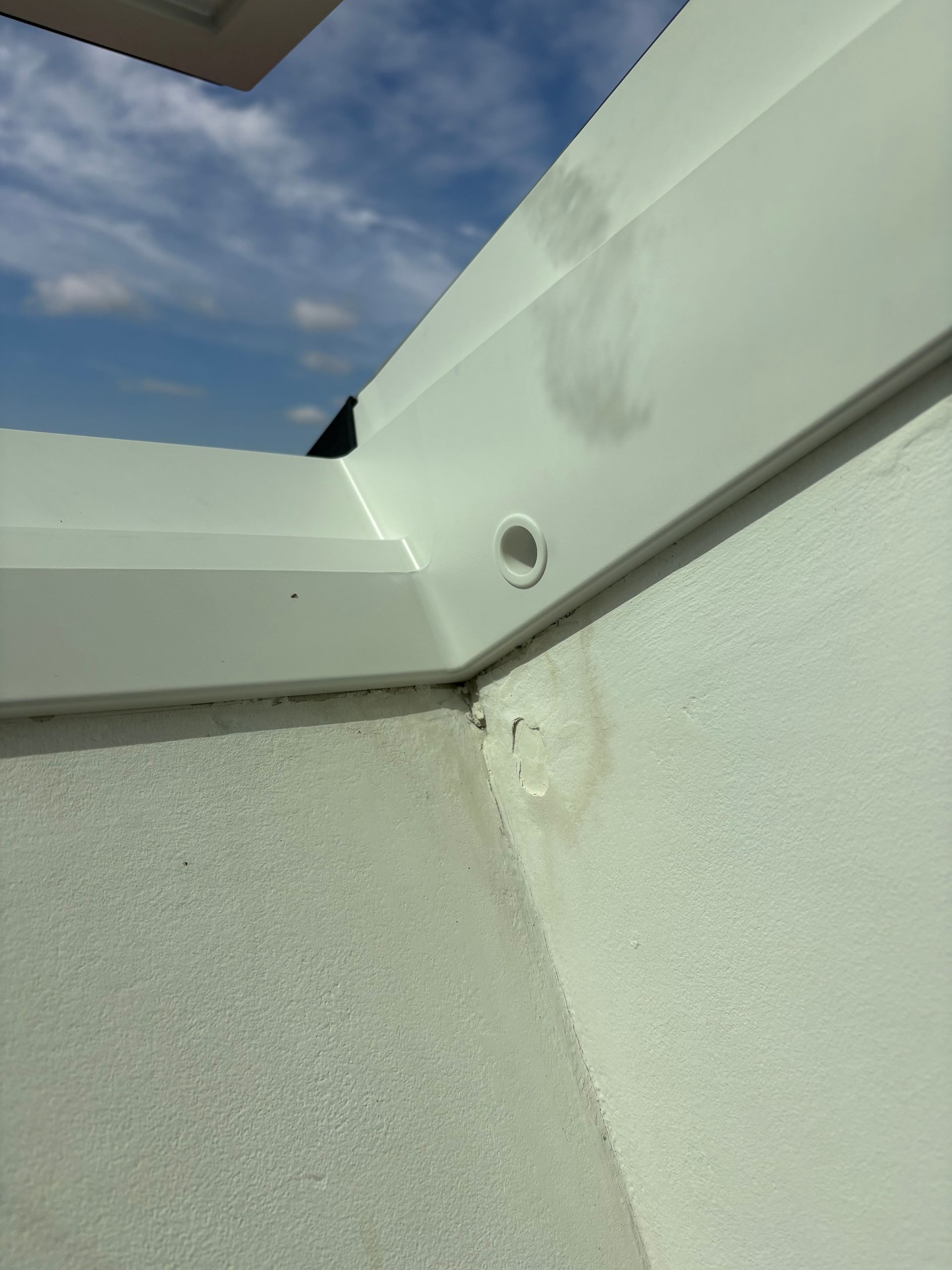 Moulure en plastique blanc sur un mur en stuc, percée d'un petit trou rond, sur fond de ciel bleu.