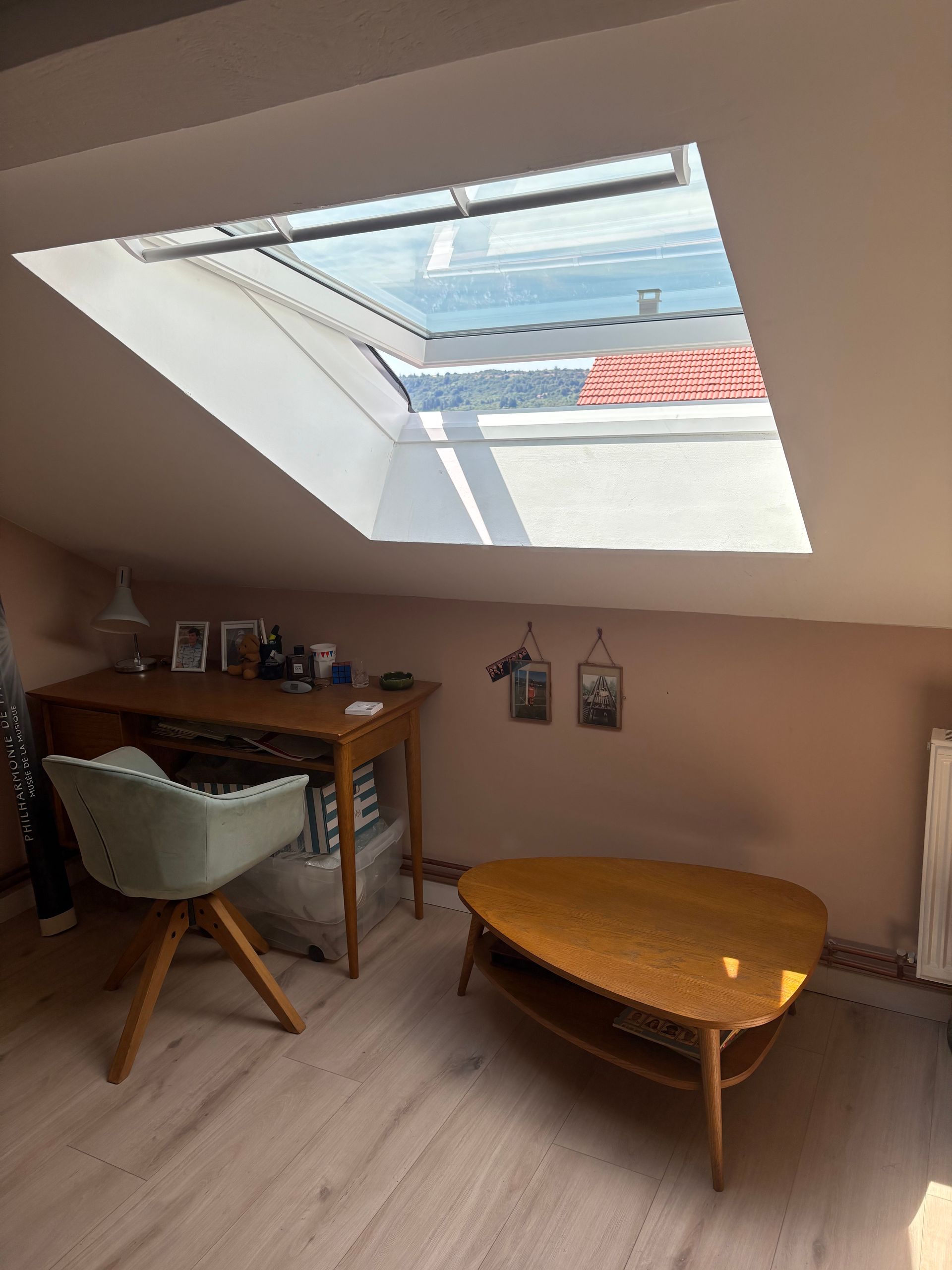 Pièce mansardée avec un bureau, une chaise et une table basse sous une lucarne.