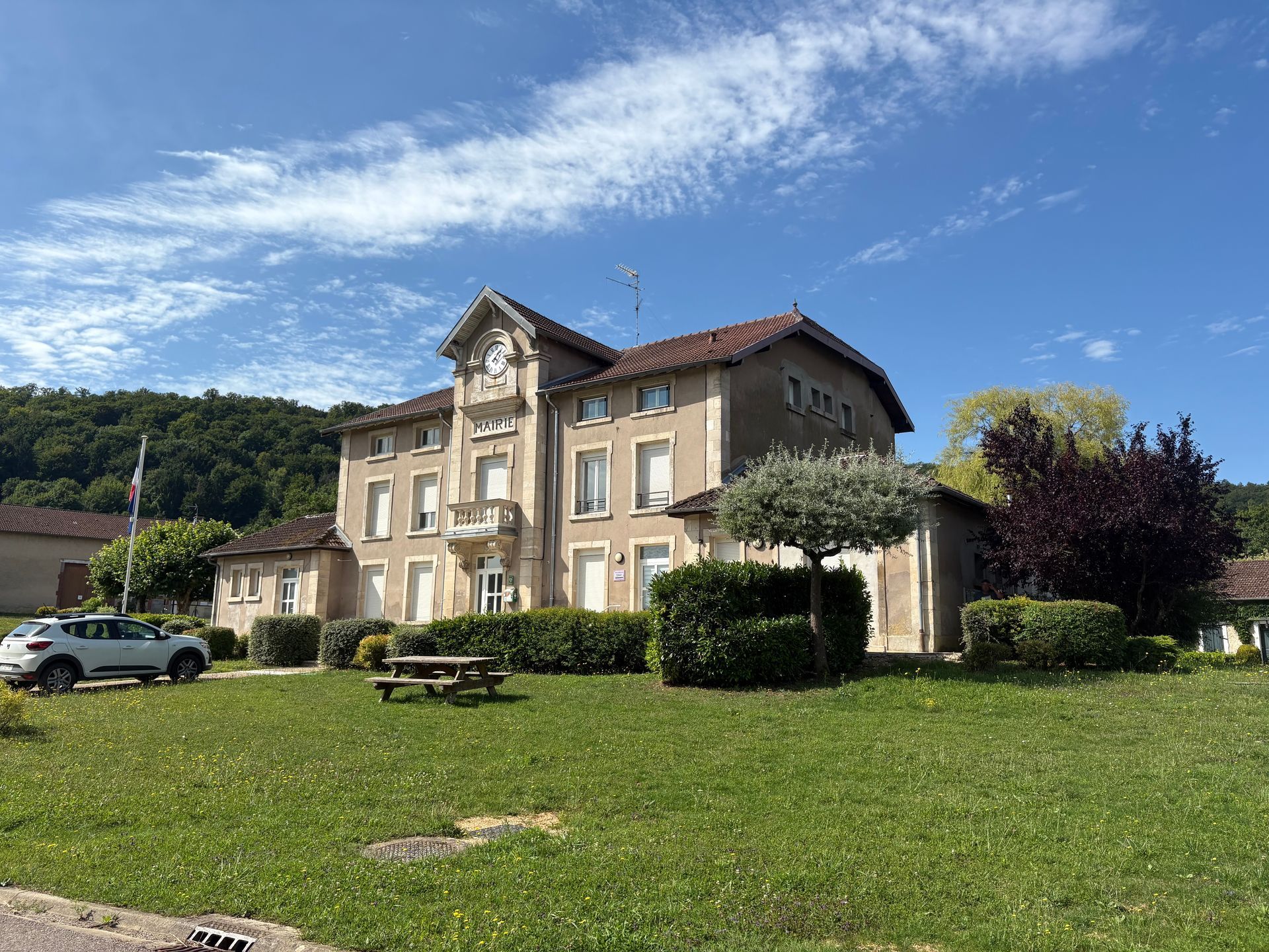 Bâtiment avec une horloge en façade, entouré d'une pelouse et d'arbres, sous un ciel bleu.