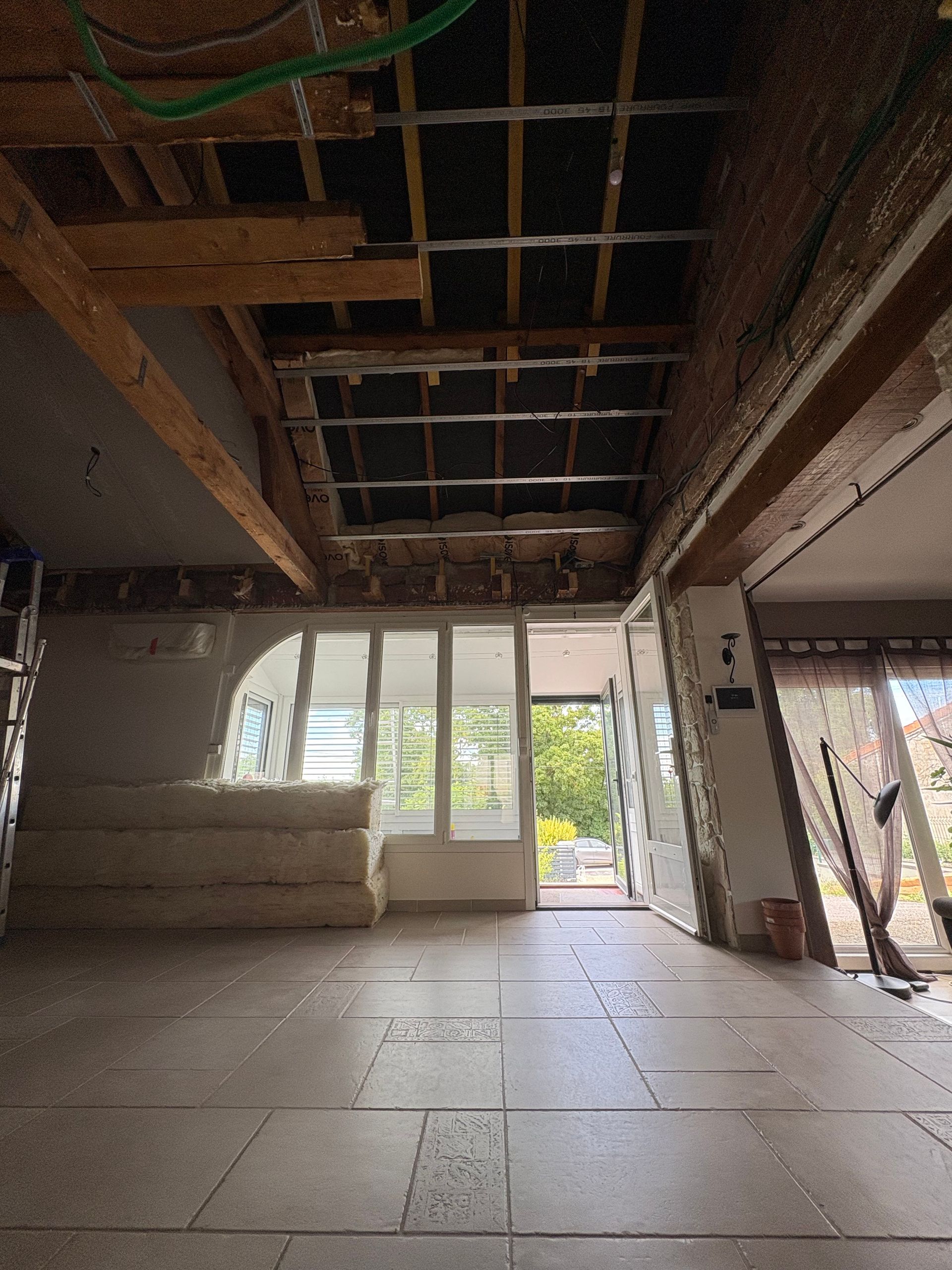 Vue intérieure d'une pièce en construction, avec poutres apparentes, isolation et sol non fini. 