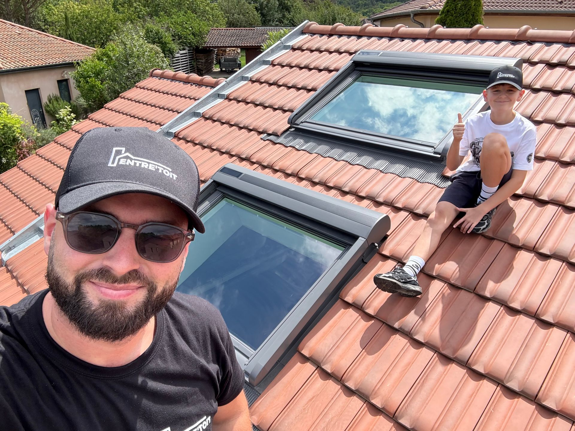 Un homme et un enfant sur un toit de tuiles percé de puits de lumière, l'un d'eux faisant un signe d'approbation.
