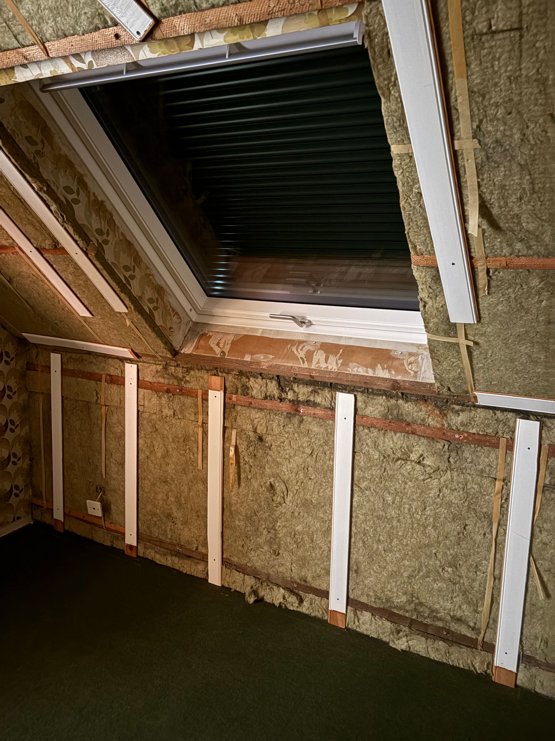 Vue intérieure d'un grenier isolé avec un puits de lumière. L'isolant brun est visible le long des murs.